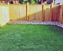 Artificial grass in backyard with stone edge along fence